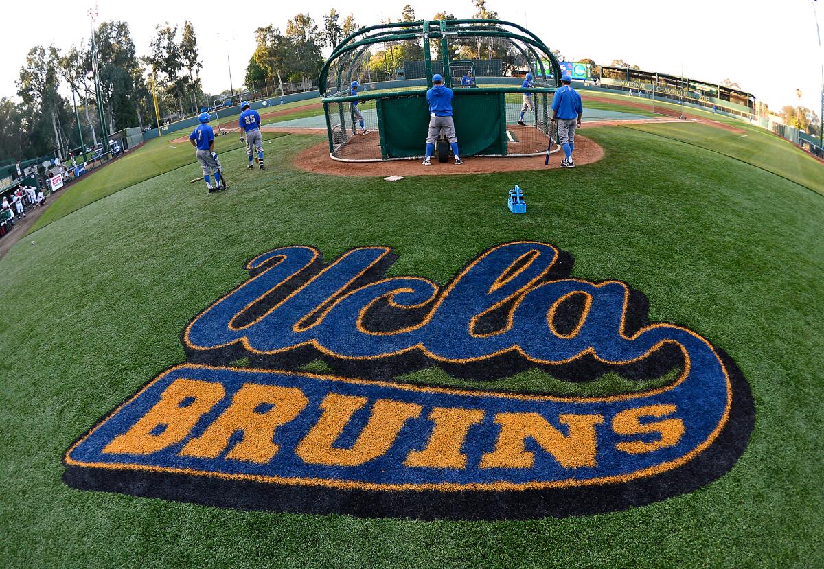 A batting cage is seen behind a UCLA Bruins logo on the grass.