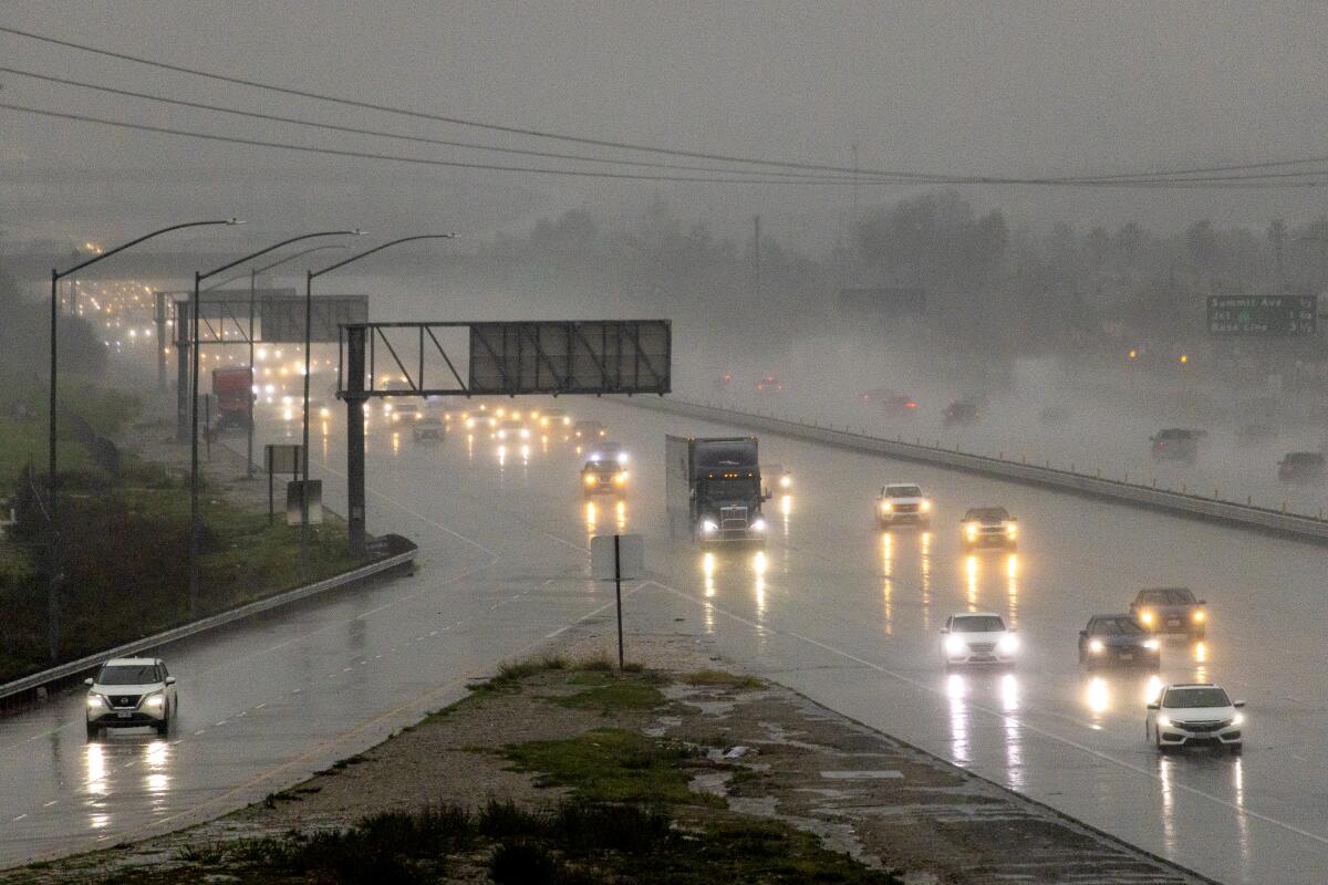 Cars and trucks drive a rainy freeway with their headlights on.