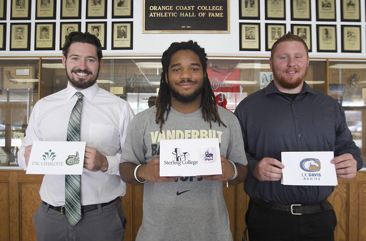 OCC football players, from left, tight-end-fullback Ryan Eachus, defensive back Melvin Irby and offensive lineman Will Martin hold cards representing the colleges they will transfer to during a signing ceremony at OCC on Wednesday.