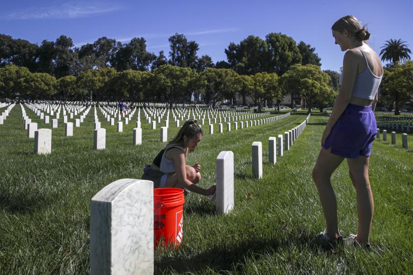 Los Angeles, CA - September 24: Allison Kim, 20, left, and Kennedy Snyder, 20, both USC students, clean veterans' headstones at Los Angeles National Cemetery on Saturday, Sept. 24, 2022 in Los Angeles, CA. (Irfan Khan / Los Angeles Times)