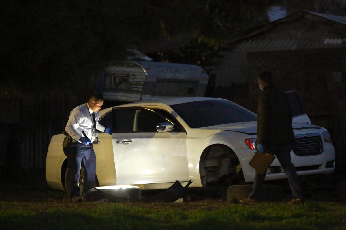Investigators shine a flashlight near a car.