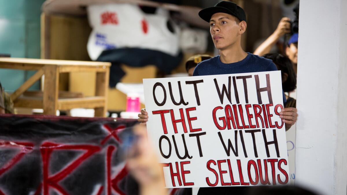 A member of an activist group holds a sign protesting Self Help Graphics and other art galleries in Boyle Heights.