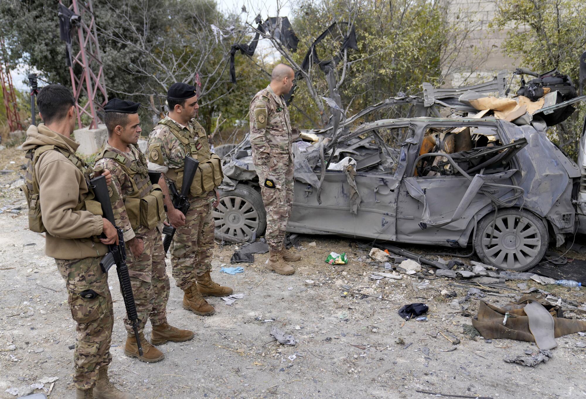 Soldiers stand next to a charred vehicle.