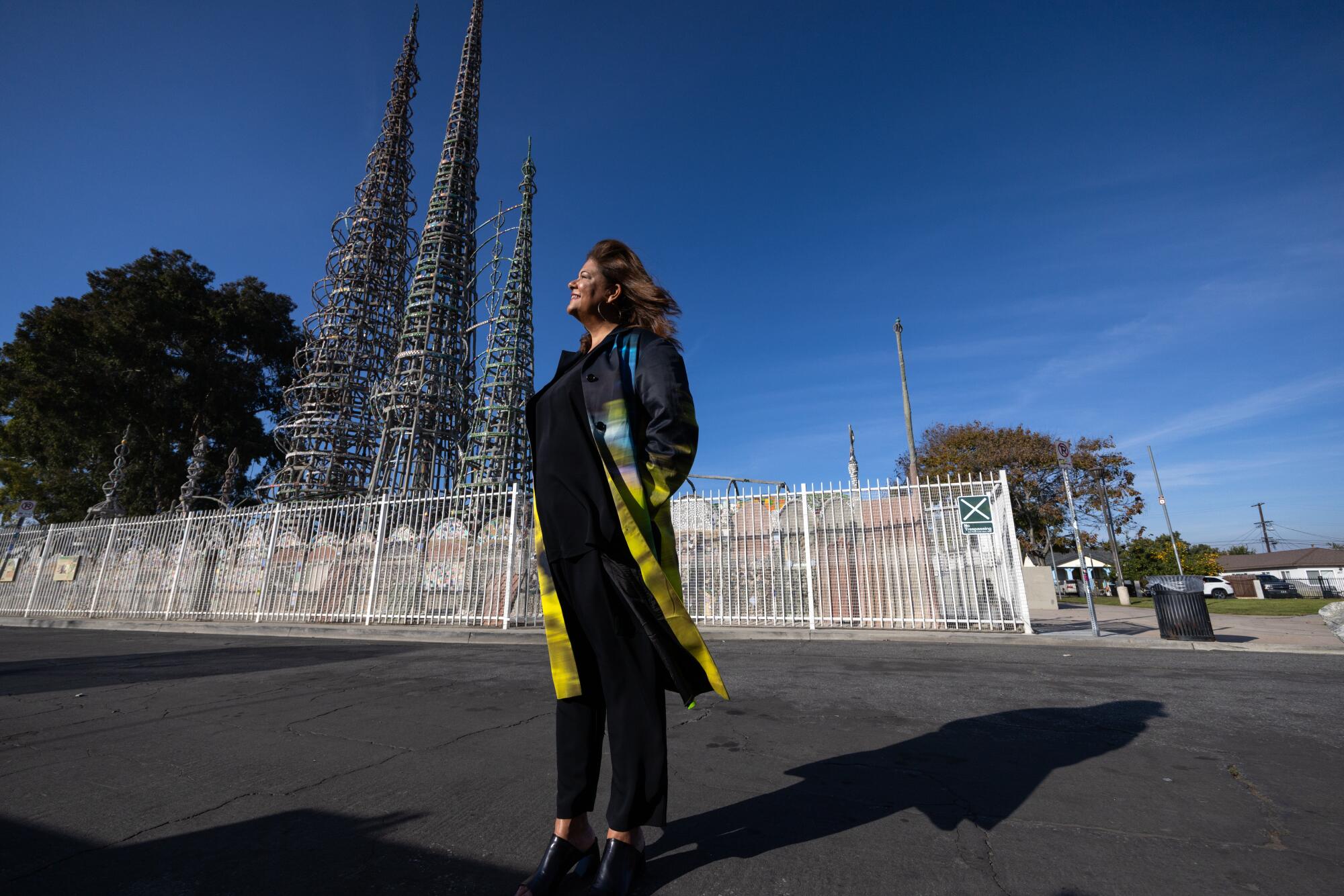 Elizabeth Alexander, a Black woman in a flowing coat, stands before the Watts Towers.