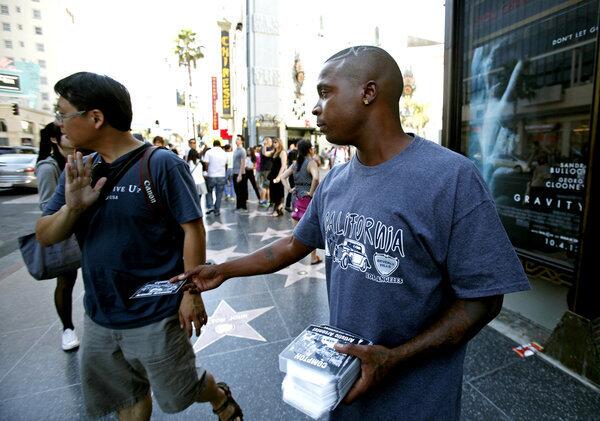 A pedestrian shuns a man who identified himself only as Najea, right. Najea hands out "free" CDs to passersby in front of the TCL Chinese Theatre in Hollywood. He could soon face a new crackdown for passing out CDs and then asking for a donation.