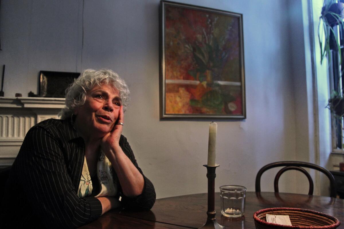 A 2010 photo shows Edith Grossman seated a dining table, a painting behind her, looking thoughtful.