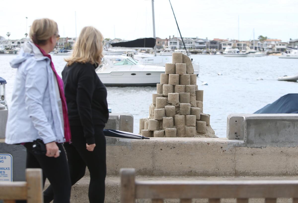 Passersby view sandcastle artist Chris Crosson's toilet paper tower titled "Roll With It" on Balboa Island in Newport Beach on Monday — a lighthearted take on the coronavirus-related rush on toilet paper at stores.
