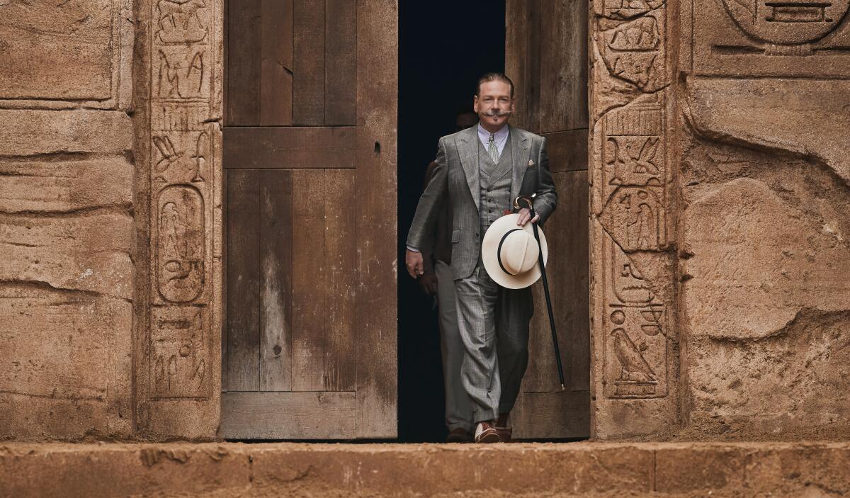 A man in a gray suit strides out of an Egyptian ruin.