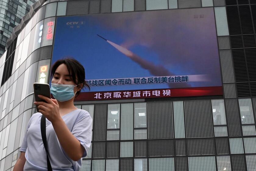A woman uses her mobile phone as she walks in front of a large screen showing a news broadcast about China's military exercises encircling Taiwan, in Beijing on August 4, 2022. - China's largest-ever military exercises encircling Taiwan kicked off August 4, in a show of force straddling vital international shipping lanes after a visit to the island by US House Speaker Nancy Pelosi. (Photo by Noel Celis / AFP) (Photo by NOEL CELIS/AFP via Getty Images)