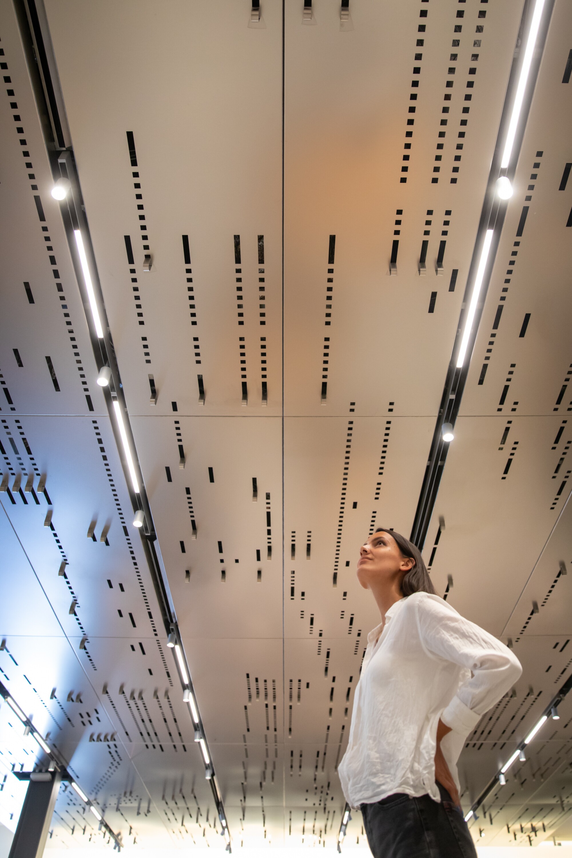A woman stands under a stainless steel ceiling canopy that has been die cut to resemble a player piano scroll.