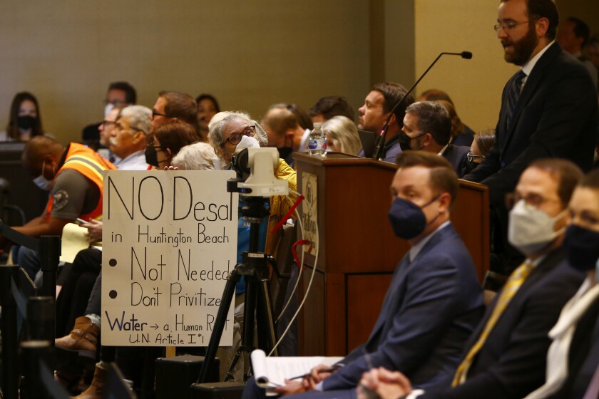A woman holds a sign opposing a desalination plant in Huntington Beach.