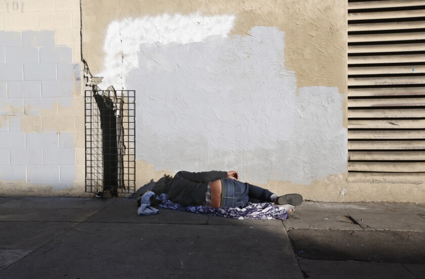 A man sleeps on the sidewalk on 16th Street in San Diego on Dec. 16, 2019.