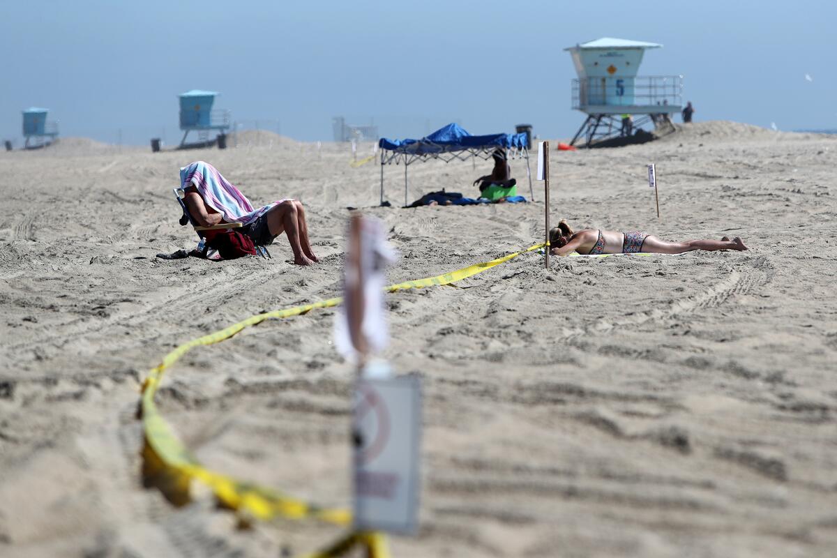 A sunbather lies between signs warning visitors of the oil spill on the south side of Huntington Beach Pier on Tuesday.