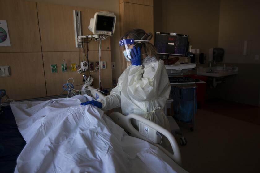 MISSION HILLS, CA - DECEMBER 31: A patient has died inside the COVID ICU at Providence Holy Cross Medical Center on Thursday, Dec. 31, 2020 in Mission Hills, CA. Wearing a yellow isolation gown, mask, gloves, and a face sheild Chaplain Anne Dauchy places her right hand gentley on the body covered by a white body bag as she talks with the family of the patient. (Francine Orr / Los Angeles Times)