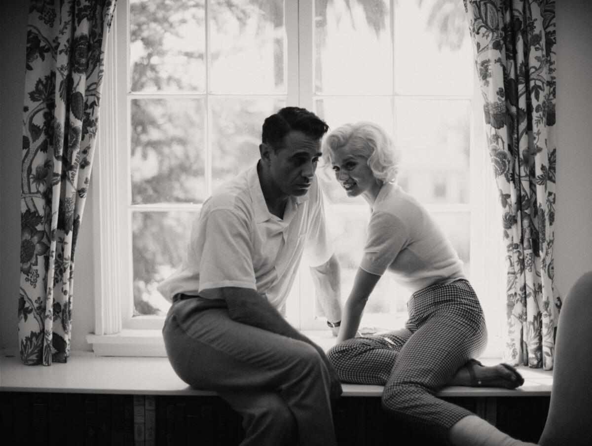 A man and a woman sit in front of a window  in the movie "Blonde."