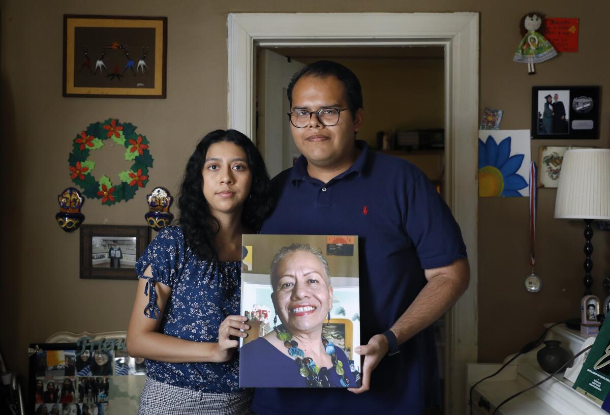 A woman with dark hair, left, and a man with dark hair and glasses hold a portrait of a smiling woman 