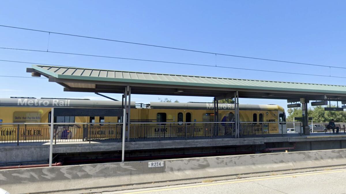 A train with the words "Metro Rail" sits at a station next to a freeway.