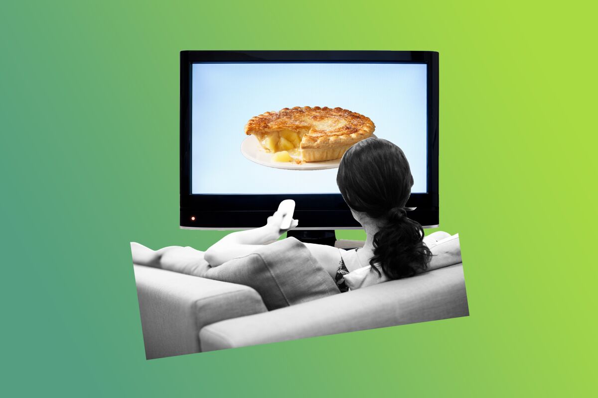 A woman sits on a couch looking at a pie on her television. 