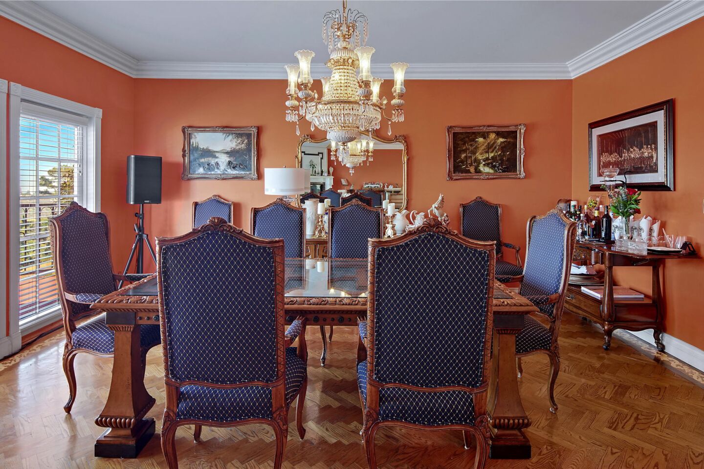 The dining room has orange walls and a dining table and chairs overlooking a window.