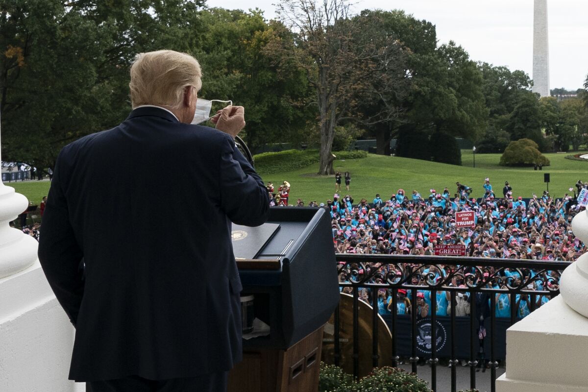 President Trump removes his mask before speaking to a crowd of supporters Saturday at the White House.