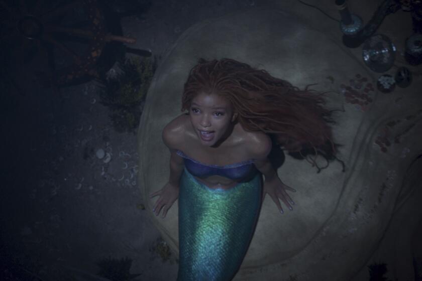 Halle Bailey, dressed as a mermaid, sings underwater while sitting on a rock.