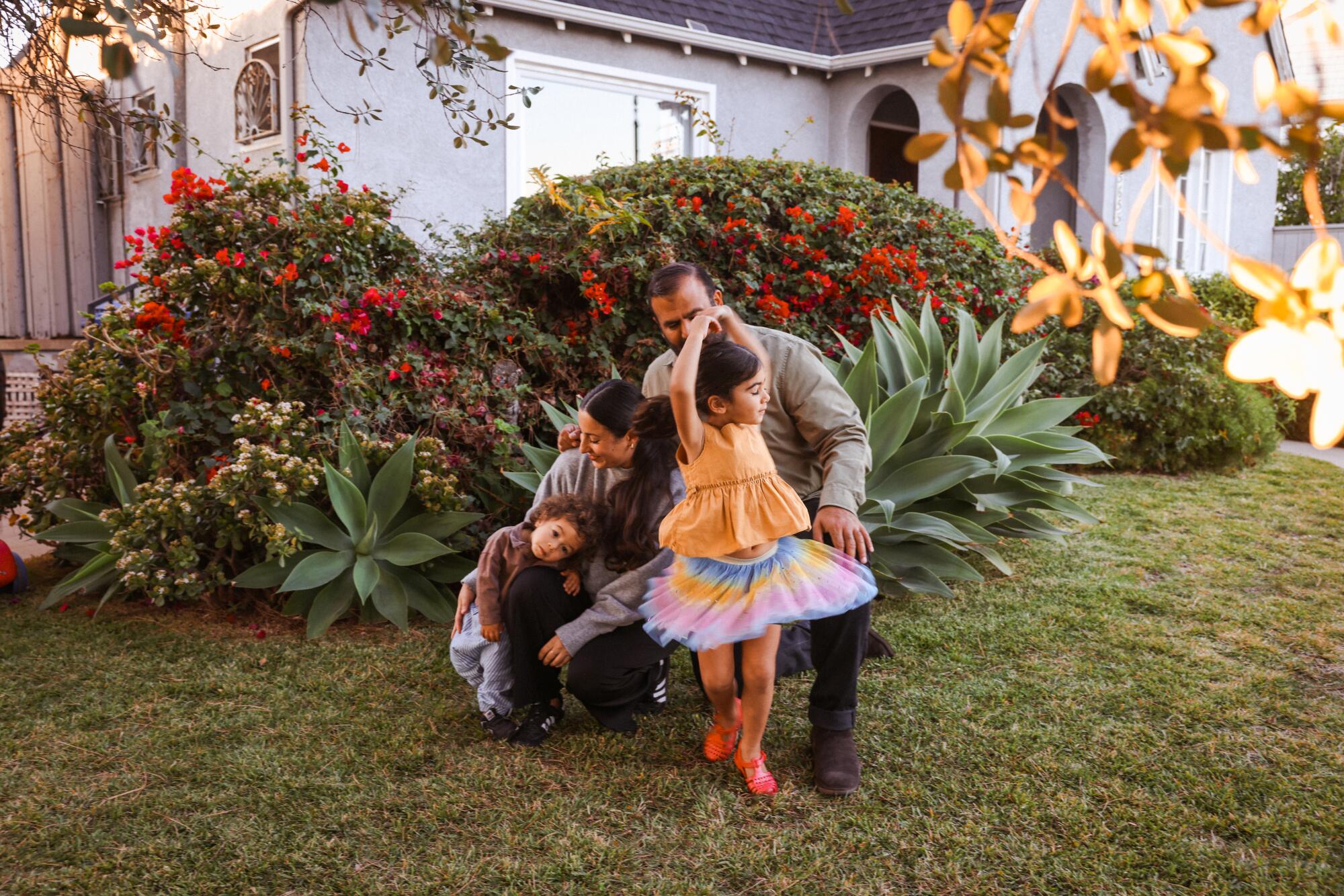 A child twirls in the yard surrounded by her parents and sibling. 
