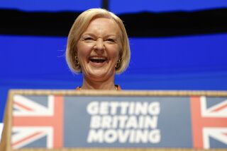 La primera ministra británica Liz Truss ríe durante su discurso en la conferencia del Partido Conservador en Birmingham, Inglaterra, miércoles 5 de octubre de 2022. La consigna en inglés dice "Poner a Gran Bretaña en movimiento". (AP Foto/Kirsty Wigglesworth)