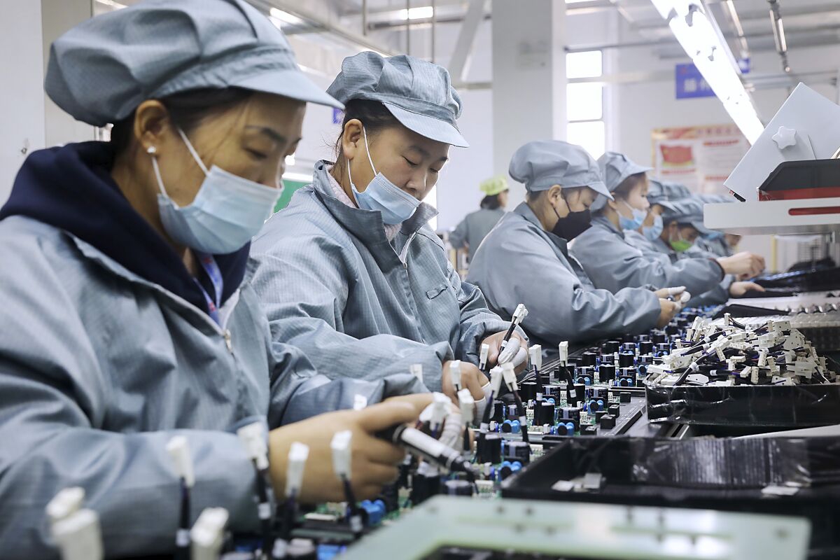 Workers wearing face masks assemble electronic parts at a factory in Huaibei in central China's Anhui Province, Monday, Nov. 29, 2021. Chinese leaders on Friday, Dec. 10, 2021 promised tax cuts and support for entrepreneurs next year to shore up slumping economic growth after a campaign to rein in surging corporate debt caused bankruptcies and defaults among real estate developers. (Chinatopix via AP)