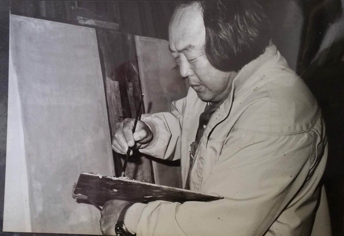 A Japanese man with shoulder-length hair dips a brush into his painter's palette.