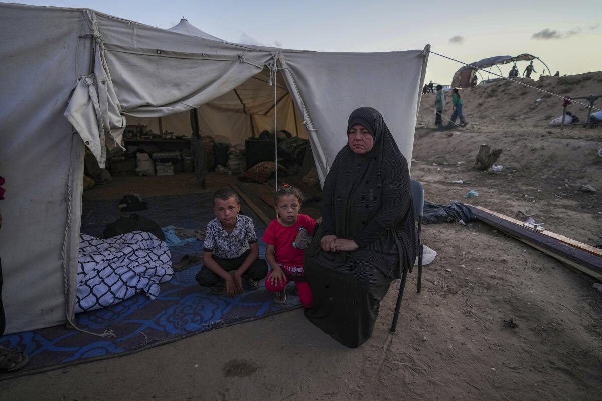 A Palestinian woman sits in front of a tent with her grandchildren.