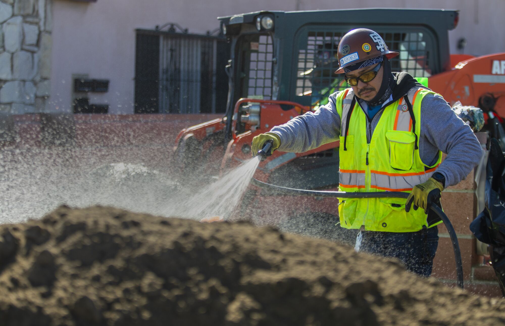 A worker sprays water on a pile of soil.