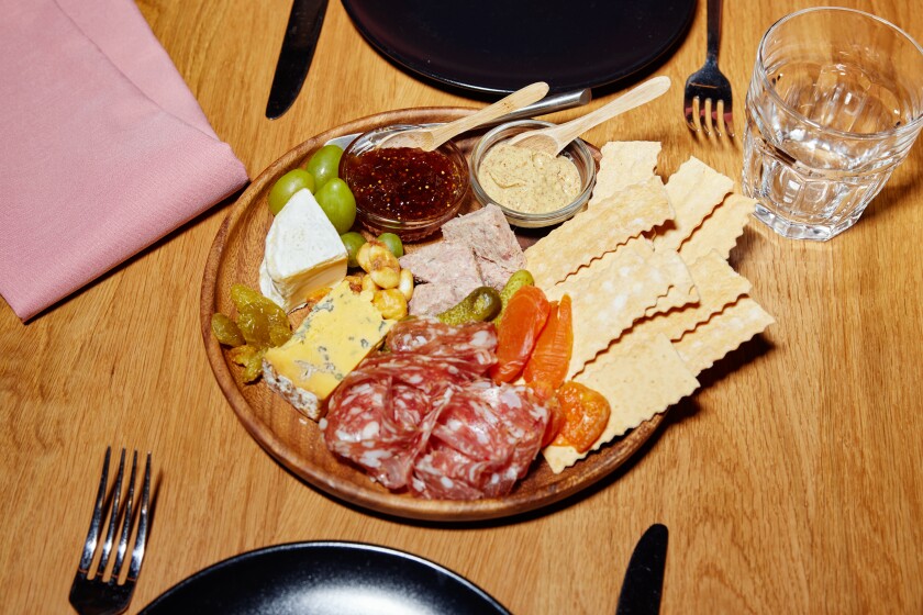 A platter arrayed with cheese, meat, crackers and spread.