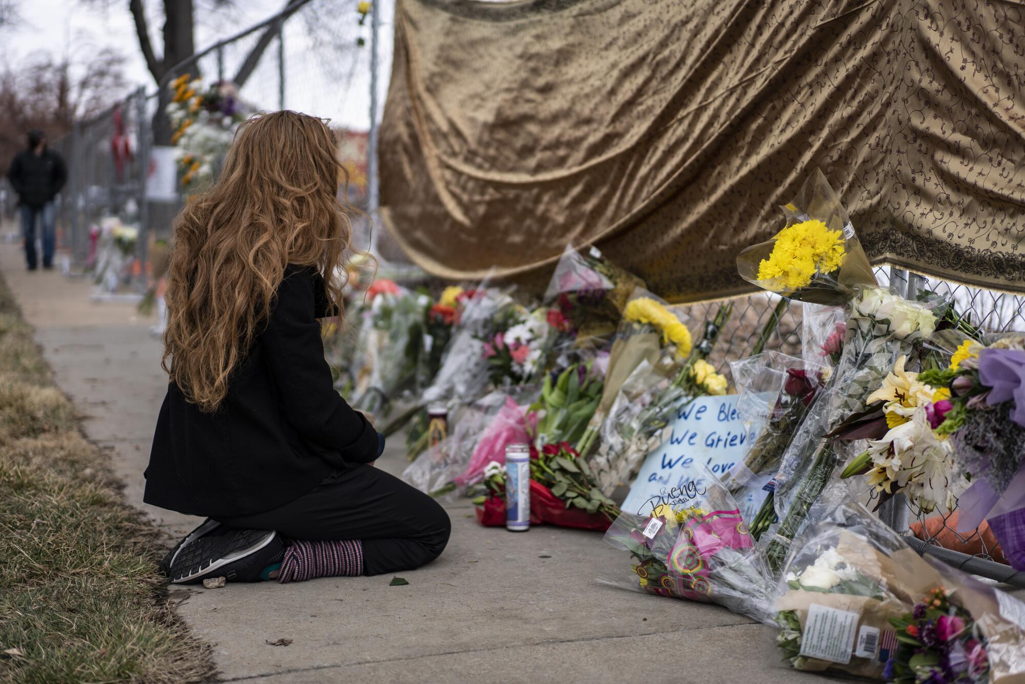 A mourner kneels before growing sidewalk memorial outside the King Soopers grocery store