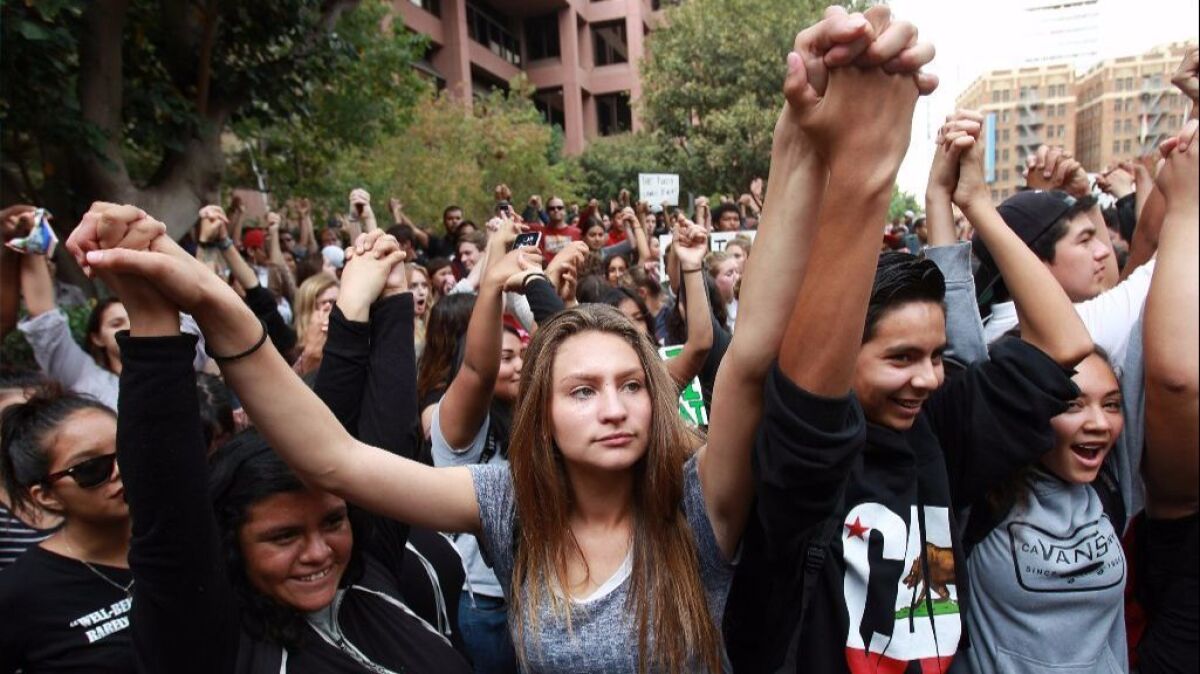 San Diego High School students Cinthia Hernandez, 16, left, Coralynn Bradley, 15, center, and Angel Casian, 15, hold their arms up as they join other students in front of the federal court building in downtown San Diego to protest Donald Trump's presidential victory.