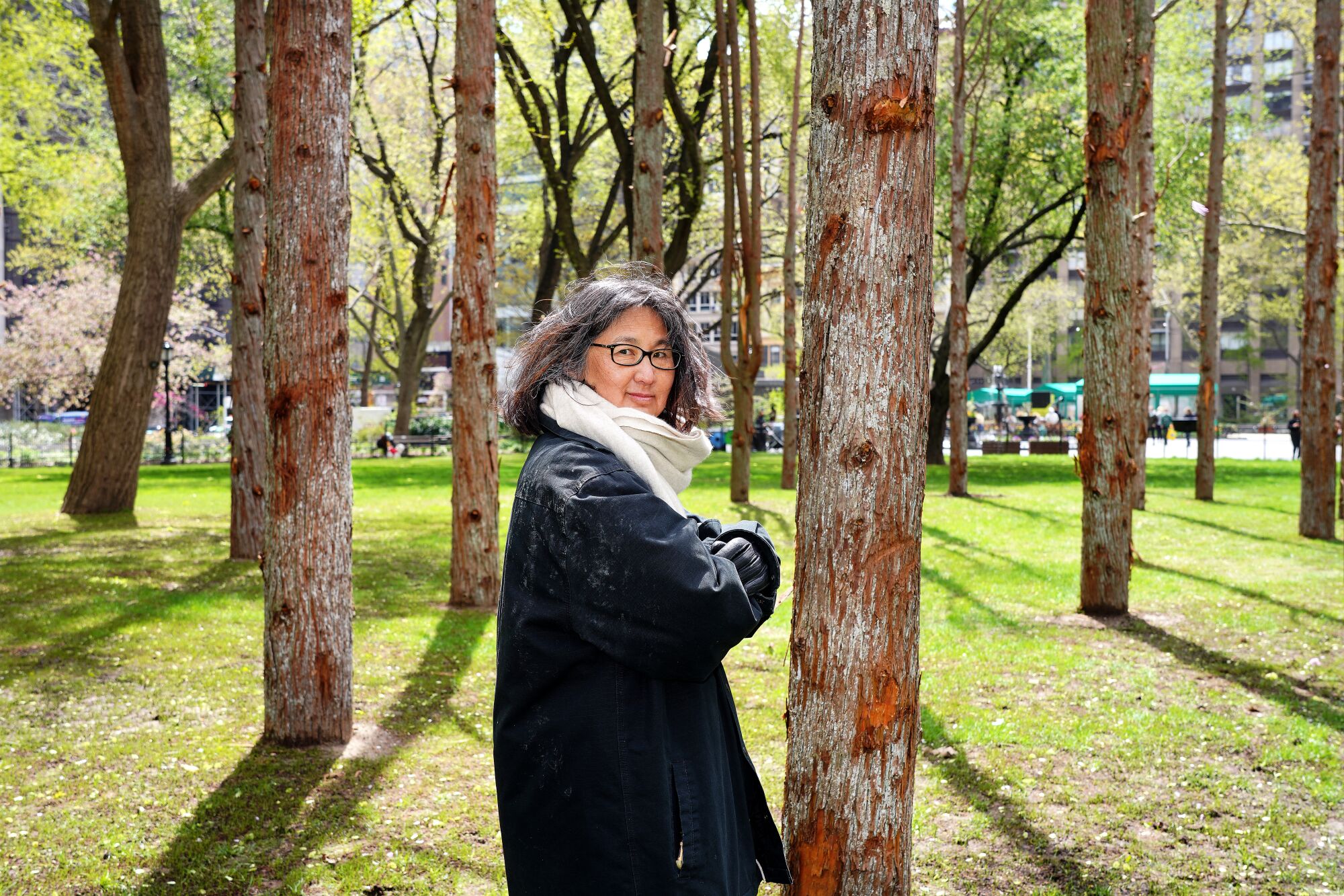 Maya Lin, in a black coat, stands amid the dead tree trunks of her "Ghost Forest" installation.