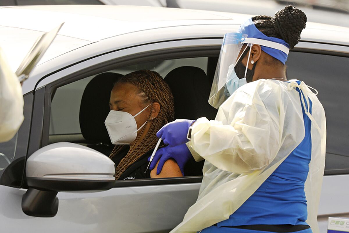 A driver closes her eyes as a health worker rolls up her sleeve to administer a vaccine shot through the window