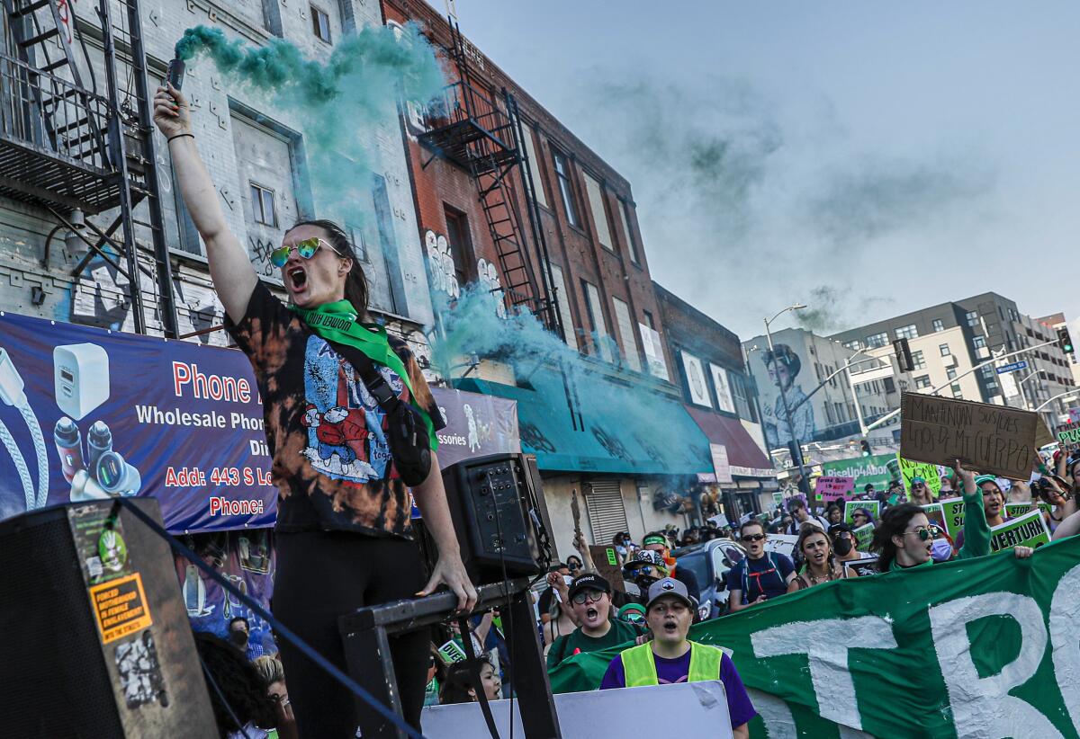 A woman holds a green flare as people rally around her.