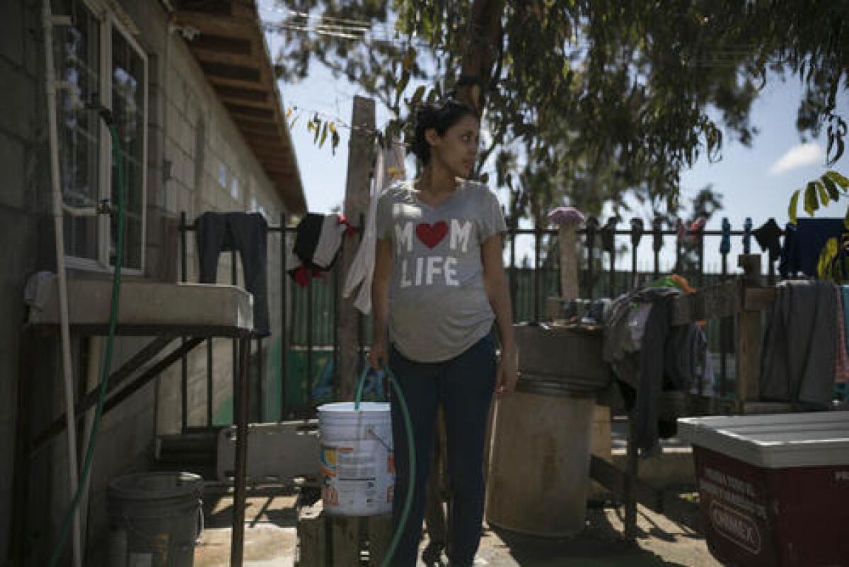 En esta imagen del 23 de mayo de 2019, la adolescente migrante embarazada Milagro de Jesús Henríquez Ayala llena un cubo con agua en el refugio de la iglesia Ágape Misión Mundial en Tijuana, México.