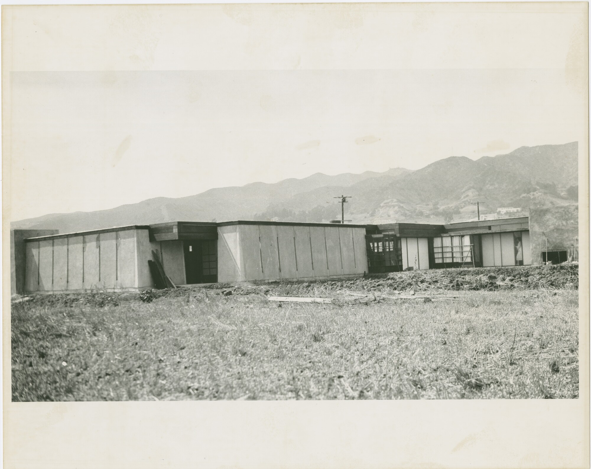 A vintage black-and-white image shows a house in a scrubby lot.