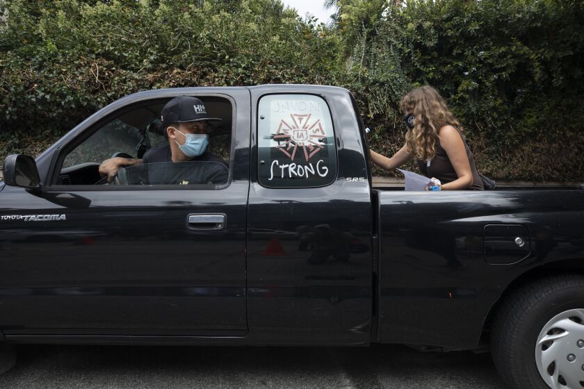 LOS ANGELES, CA - SEPTEMBER 26: Kevin Chiu of IATSE Local 80, the grip union, waits in his car as volunteer Liz Lipschultz writes pro-labor slogans on his car during a rally at the Motion Picture Editors Guild IATSE Local 700 on Sunday, Sept. 26, 2021 in Los Angeles, CA. Up to 60,000 members of the International Alliance of Theatrical Stage Employees (IATSE) might go on strike in the coming weeks over issues of long working hours, unsafe conditions, less pay from streaming companies and demand for better benefits. (Myung J. Chun / Los Angeles Times)