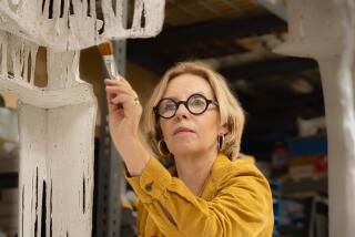 Rosa Lowinger, an art restorer and author in a mustard shirt, holds a paintbrush to an old work she is restoring.