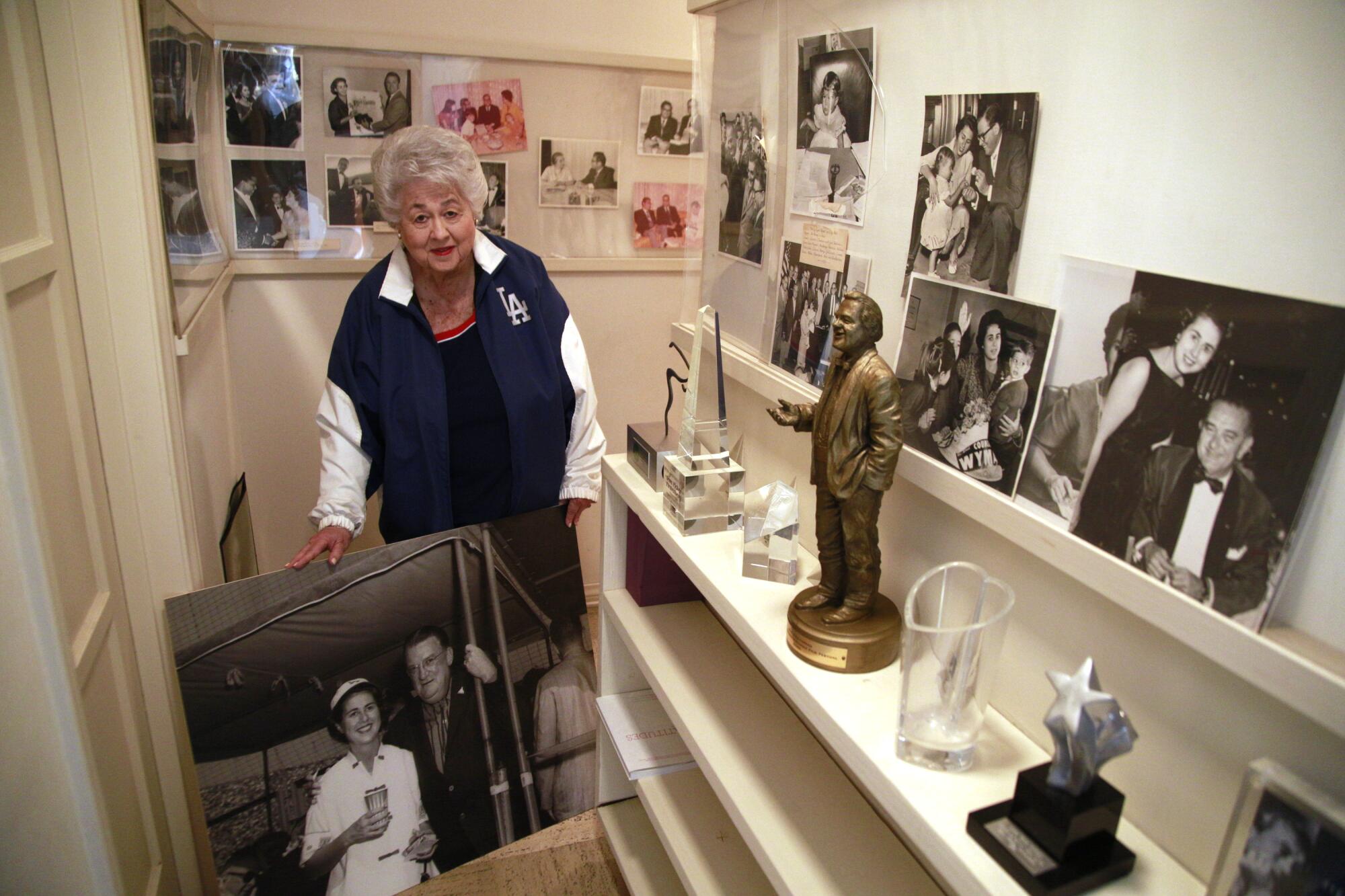 Wyman holds an enlarged photo of herself and a man while standing near other photos.