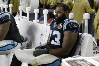 Michael Oher sitting on a bench in a black and light blue football uniform. 