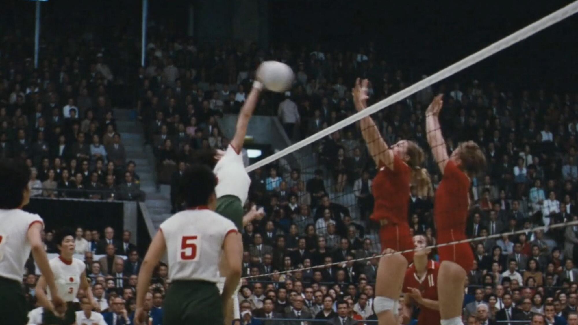 A volleyball player soars above the net to spike a ball 