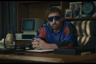 Ben Affleck in a blue and red windbreaker and big sunglasses sitting behind a desk with his hands crossed
