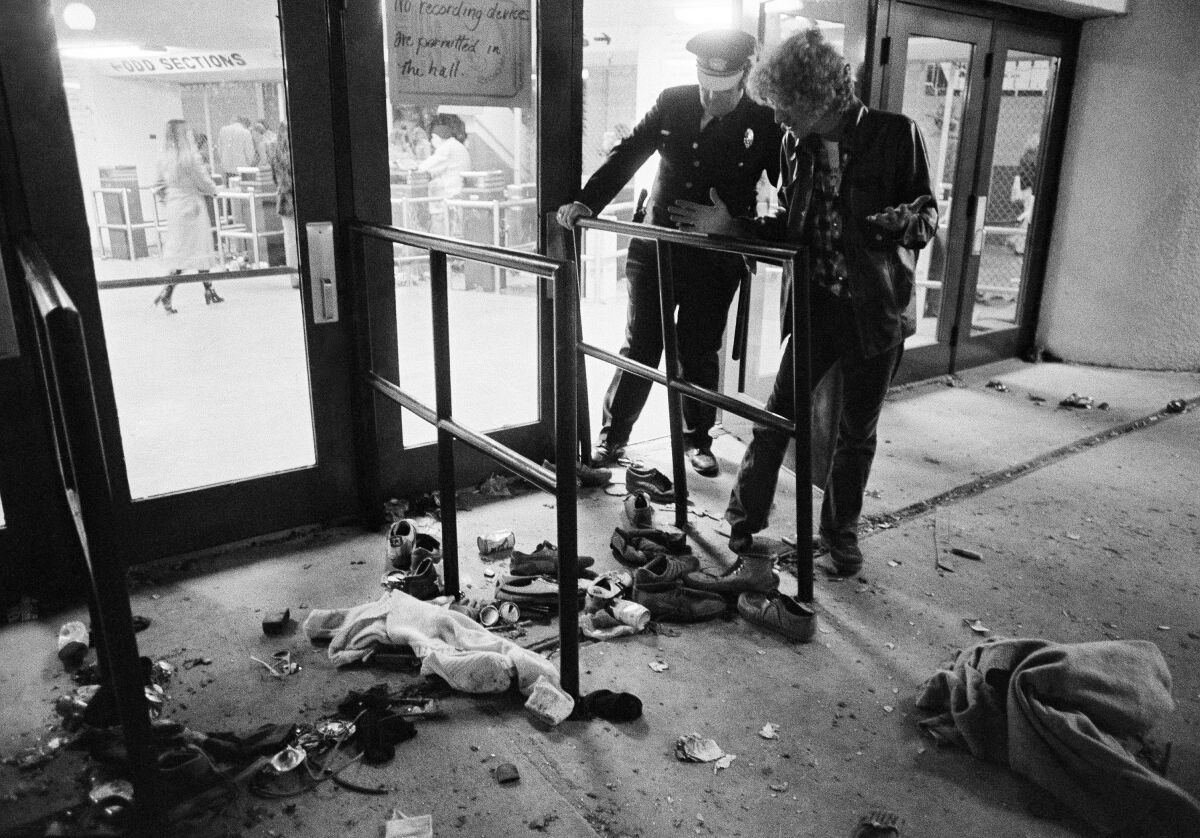 FILE - A security guard and an unidentified man look at an area with shows and clothes strewn around where several people were killed and others injured, as they were caught in a surging crowd entering Cincinnati's Riverfront Coliseum for a Who concert on Dec. 3, 1979. The crowd deaths at a Houston music festival on Friday, Nov. 5, 2021, have added to the long list of people who have been crushed at a major event. Such tragedies have been occurring around the world for a long time at concerts, sports events and religious gatherings. (AP Photo/Brian Horton, File)