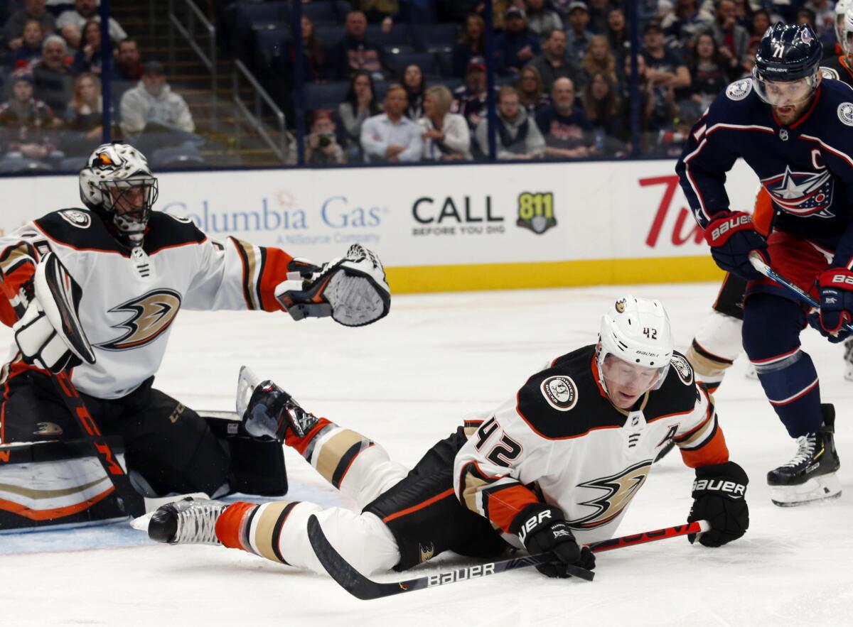 Ducks defenseman Josh Manson, center, tries to control the puck in front of goalie Ryan Miller and Blue Jackets forward Nick Foligno on Friday night.