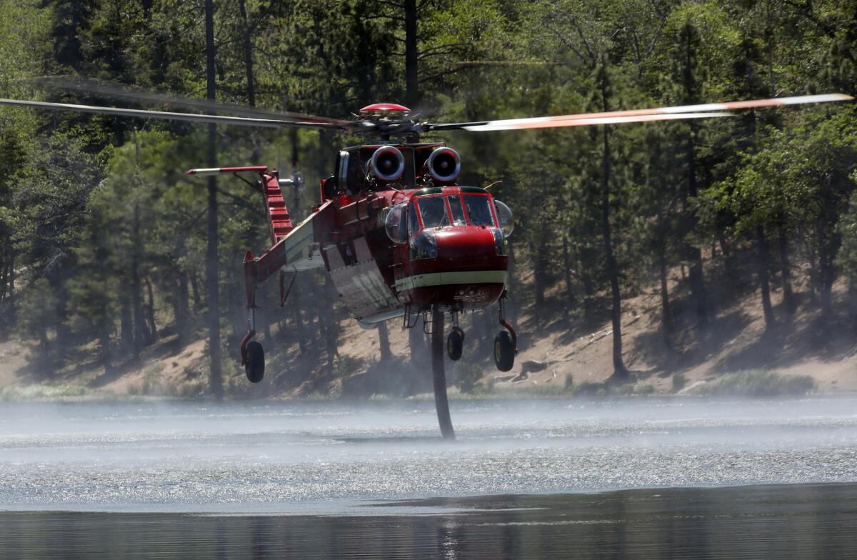 A firefighting helicopter sucks up water from Jenks Lake as it works to control flames in the Lake fire in the San Bernardino National Forest.