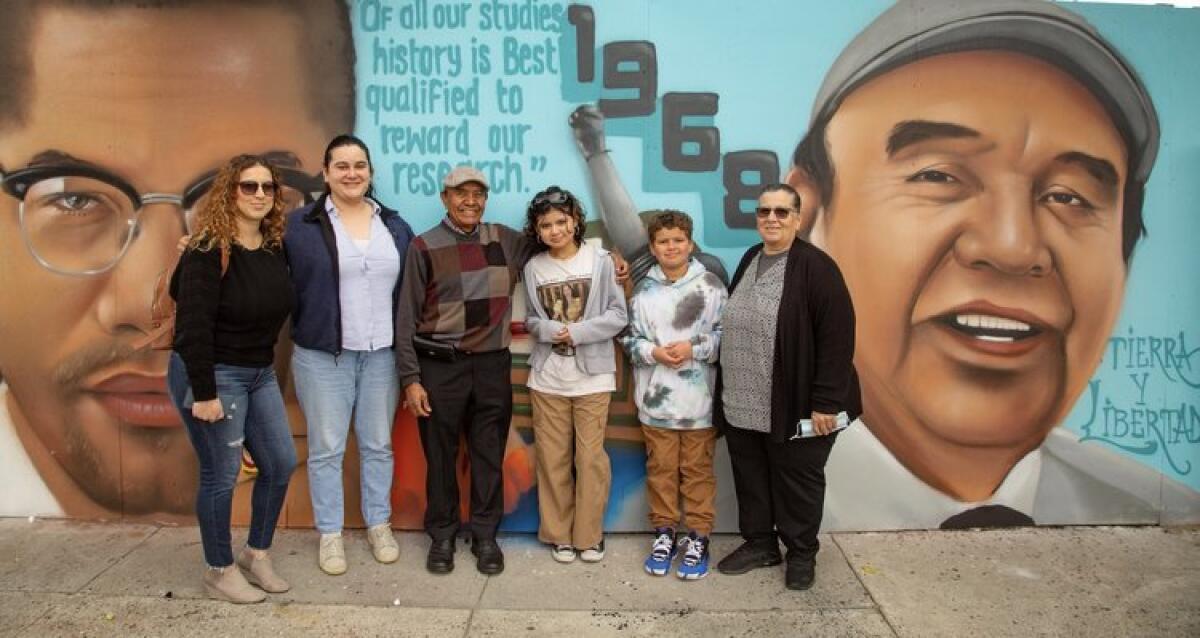 Arturo Ybarra, center, poses with family and friends in front of a mural featuring his likeness in Watts.