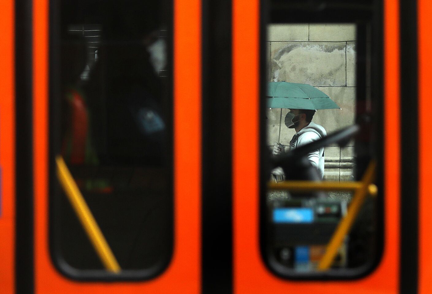 A bus driver and a pedestrian wear protective masks on a rainy day in downtown Los Angeles.